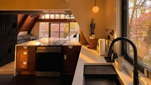 A modern kitchen with a central island, a built-in oven, and a window with a view of cherry blossoms. - Custom A-Frame | Lake Access • Fire Pit (Highland Lakes)