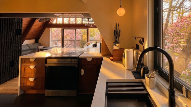 Uma cozinha moderna com uma ilha central, forno embutido e janela com vista para cerejeiras em flor.