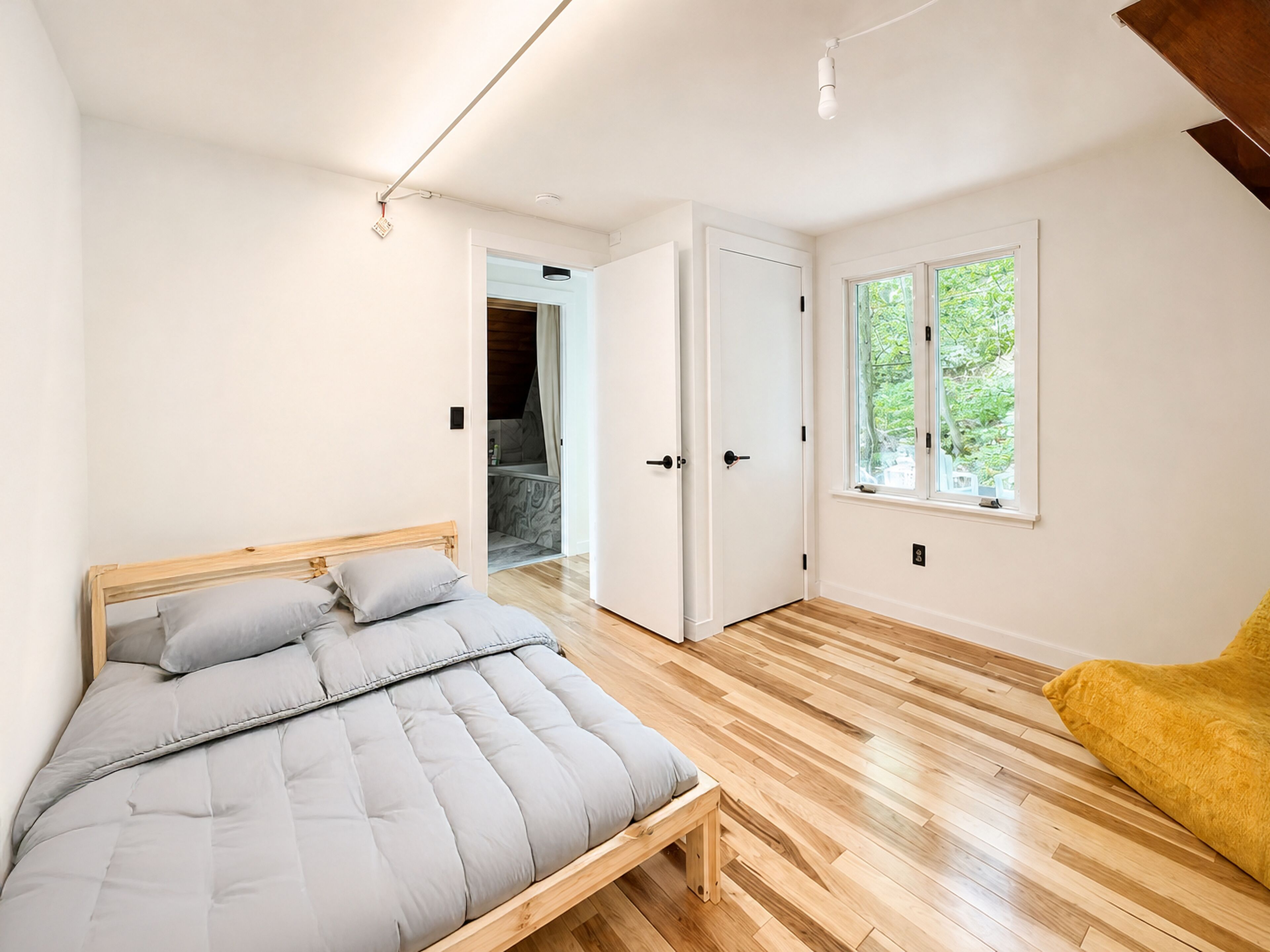 A bedroom with a bed, a wooden floor, a window, and a door.