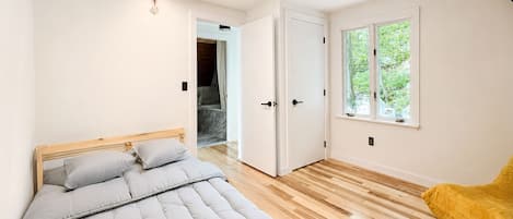 Un dormitorio con una cama, piso de madera, una ventana y una puerta.