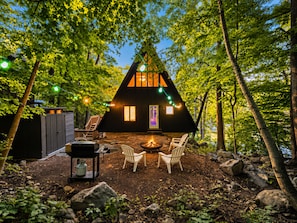 A cabin with a fire pit, outdoor seating, and string lights.