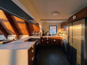 A modern kitchen with a central island, wooden ceiling beams, and a stainless steel refrigerator. - Custom A-Frame | Lake Access • Fire Pit (Highland Lakes)