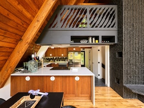 A modern kitchen with wooden accents, a central island, and a view into the dining area. - Custom A-Frame | Lake Access • Fire Pit (Highland Lakes)