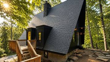 A cabin with a steeply pitched roof, wooden deck, and a stone pathway.