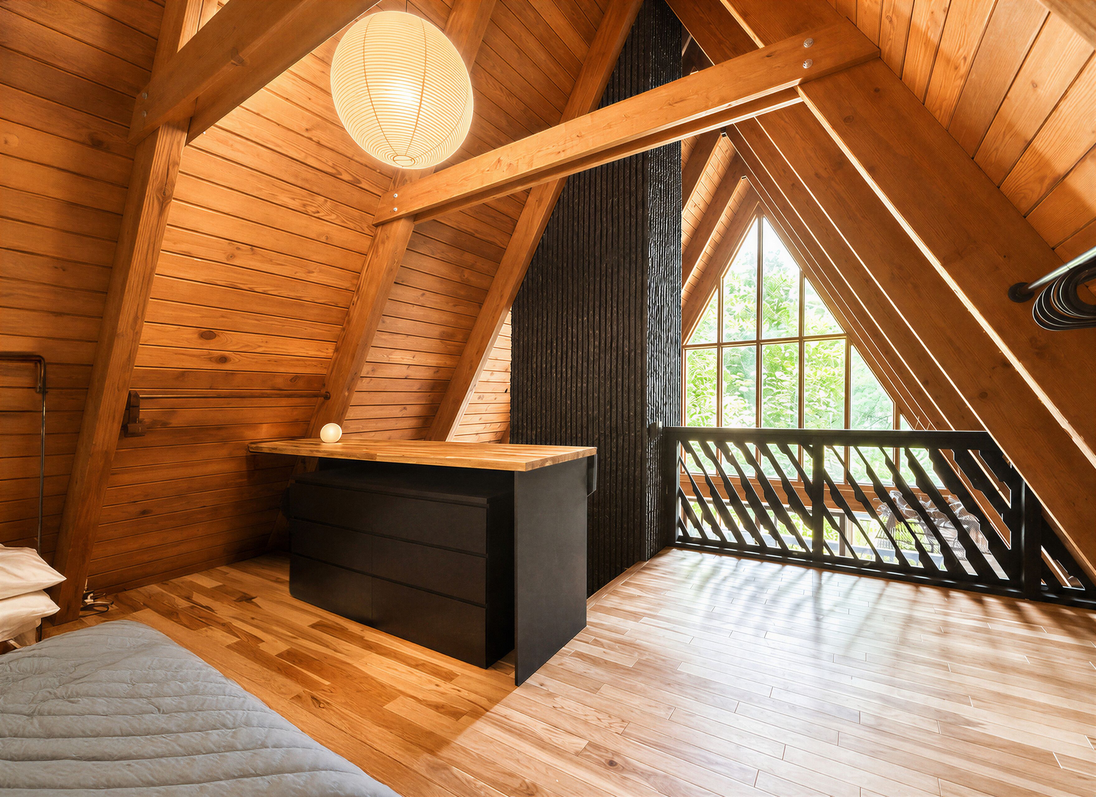Un dormitorio estilo ático con cama tipo litera, un escritorio pequeño y un ventanal grande.