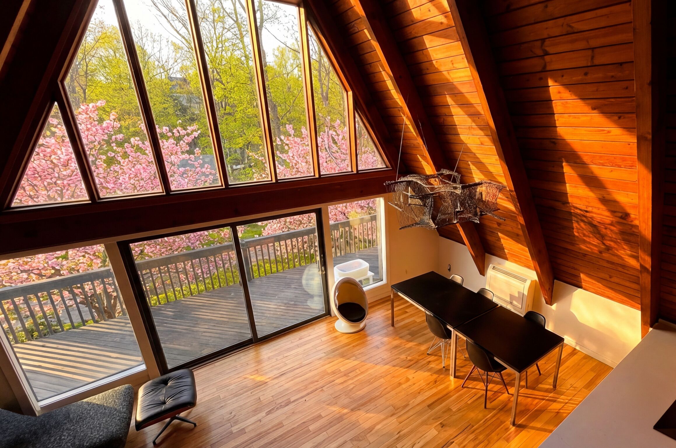 A room with a large window, wooden flooring, a table, chairs, a radiator, and a hanging light fixture.