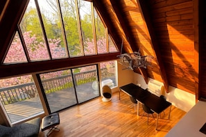 A room with a large window, wooden flooring, a table, chairs, a radiator, and a hanging light fixture.