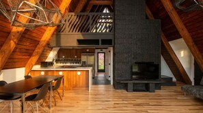A modern loft-style interior with a wooden ceiling, a kitchen area, a dining space, and a fireplace. - Custom A-Frame | Lake Access • Fire Pit (Highland Lakes)