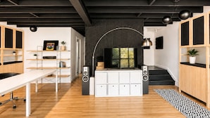 Um interior moderno com área de estar central, televisão de tela plana e escada para um andar superior.