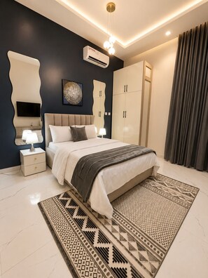Une chambre moderne comprenant un lit, des tables de chevet, un téléviseur, un appareil de climatisation et une armoire.