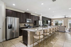 A modern kitchen with dark wood cabinets, stainless steel appliances, a granite countertop, and a bar area with stools. - PacMan, Foosball, Shuffleboard, Large Backyard, Chef Kitchen: Metropolis Estate (Kissimmee)