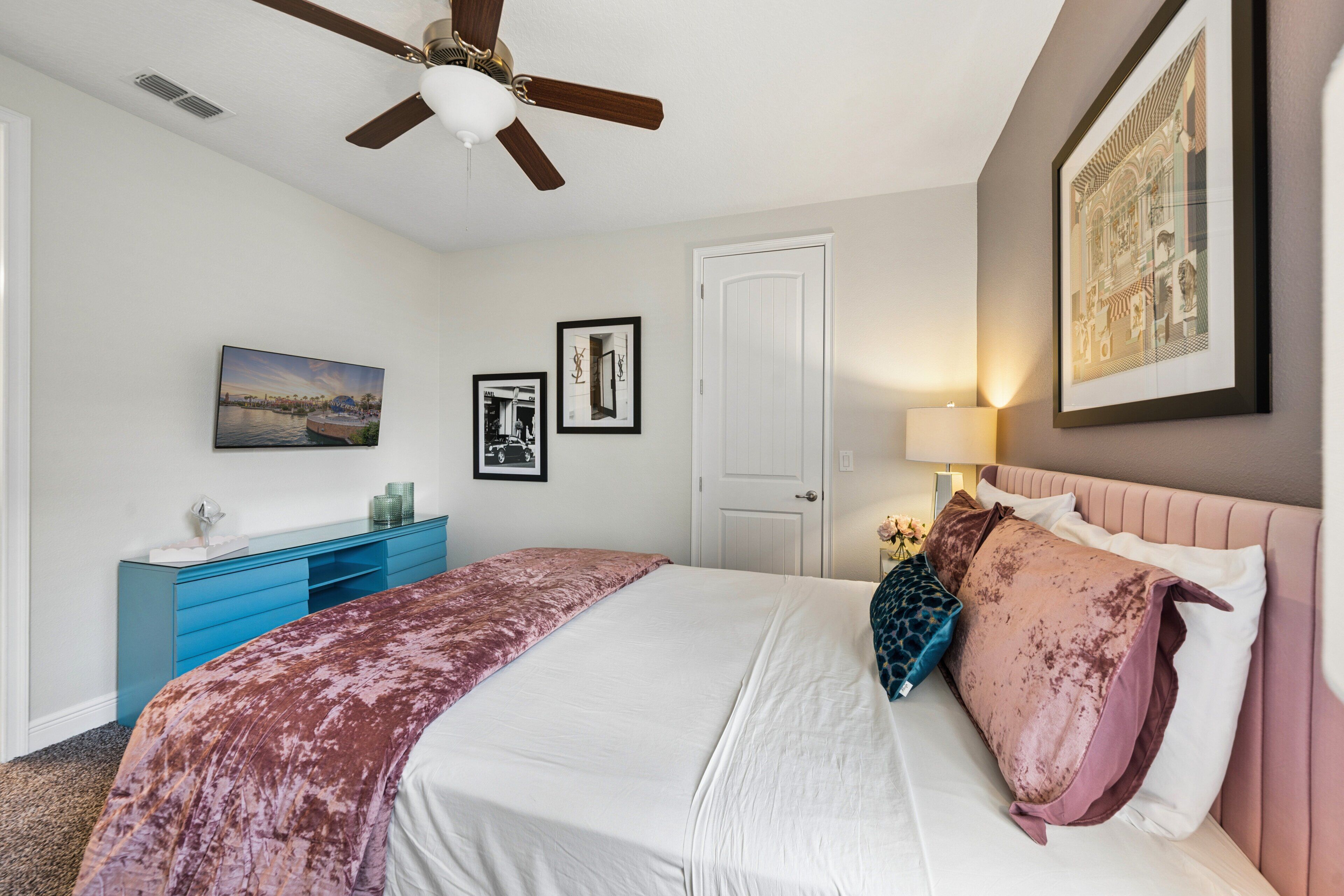 Un dormitorio con cama, ventilador de techo, cómoda y puerta.