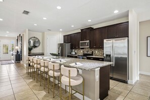A modern kitchen with a central island, bar stools, dark cabinetry, stainless steel appliances, and a tiled floor. - PacMan, Foosball, Shuffleboard, Large Backyard, Chef Kitchen: Metropolis Estate (Kissimmee)