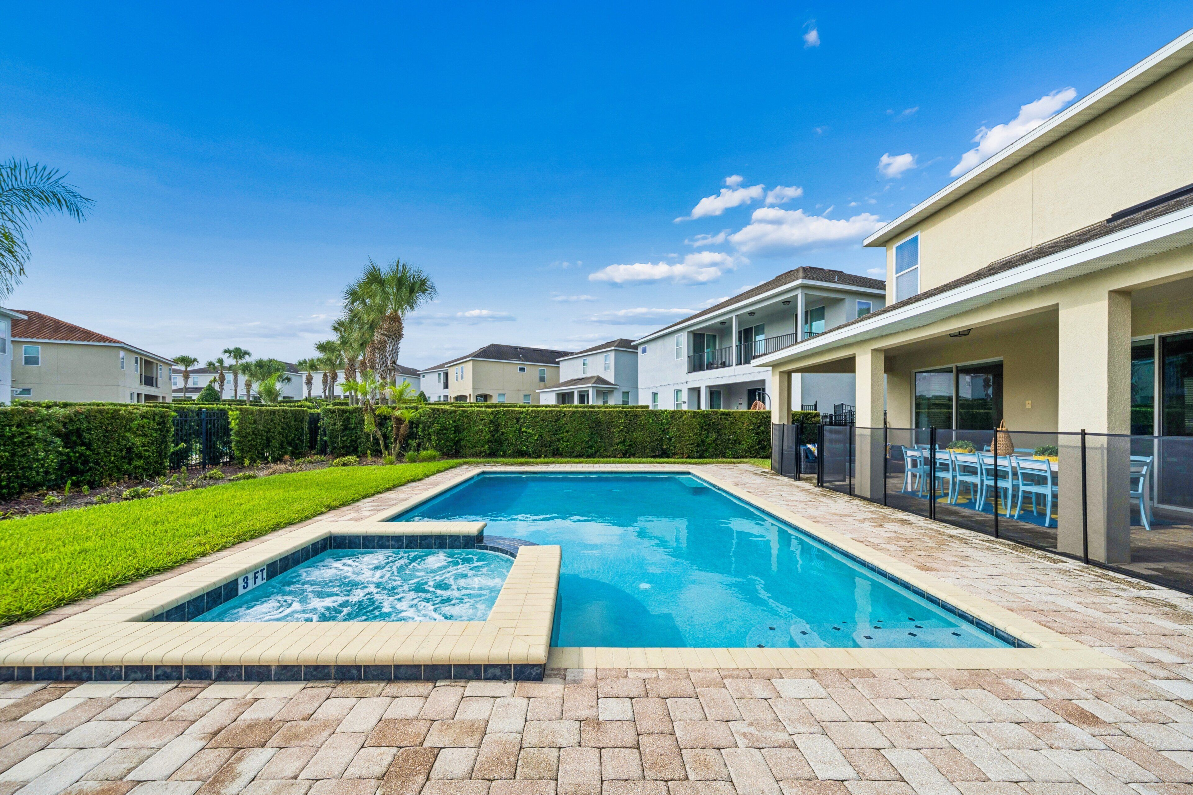A swimming pool with a hot tub, surrounded by a brick patio and a well-maintained lawn.