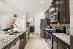 A modern kitchen with granite countertops, stainless steel appliances, and dark wooden cabinets. - PacMan, Foosball, Shuffleboard, Large Backyard, Chef Kitchen: Metropolis Estate (Kissimmee)