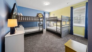 Ein Zimmer mit Etagenbetten, einem Schreibtisch, einer Lampe und einem Fenster mit Jalousien.