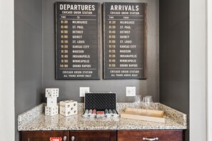 A wall-mounted departure and arrival board at a train station, with a granite countertop below displaying dice, poker chips, and glasses. - PacMan, Foosball, Shuffleboard, Large Backyard, Chef Kitchen: Metropolis Estate (Kissimmee)