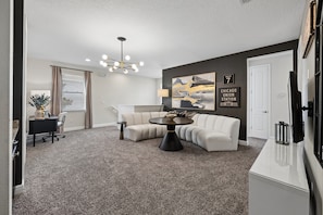 A modern living room with a sectional sofa, a round coffee table, and a chandelier. - PacMan, Foosball, Shuffleboard, Large Backyard, Chef Kitchen: Metropolis Estate (Kissimmee)
