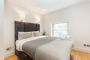 A modern bedroom with a large bed, bedside lamps, a window, and a potted plant. - Lovely 1BR Fitzrovia - Soho (London)