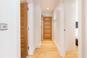 A hallway with wooden doors and white walls, leading to a room with a visible light switch. - Lovely 1BR Fitzrovia - Soho (London)
