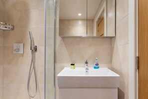 A modern bathroom with a glass shower enclosure, a white sink, and a mirror above it. - Lovely 1BR Fitzrovia - Soho (London)