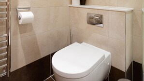 Ein modernes Badezimmer mit Toilette, Handtuchhalter, einer kleinen Ablage mit Pflanze und einem Mülleimer.