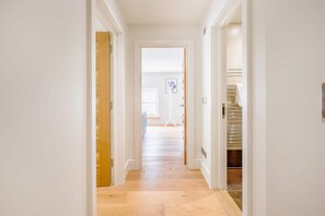 A hallway with wooden flooring, white walls, and a door leading to a room with a window. - Lovely 1BR Fitzrovia - Soho (London)