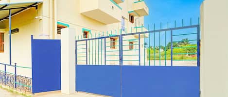Uma entrada gradeada para um edifício com esquema de cores azul e branco, um portão de metal e um céu claro ao fundo.