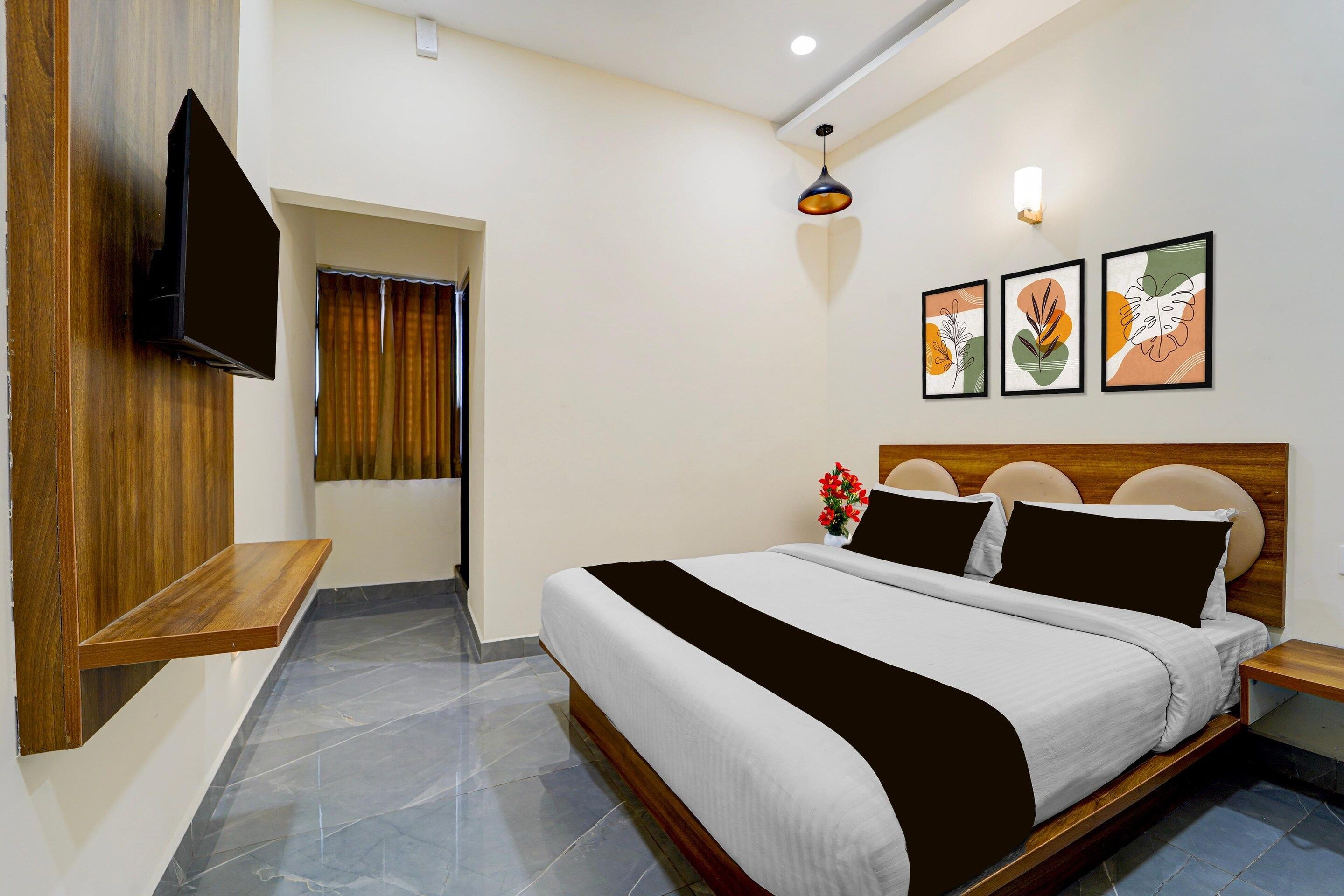 A hotel room with a bed, a TV mounted on the wall, a small wooden table, and a window with curtains.
