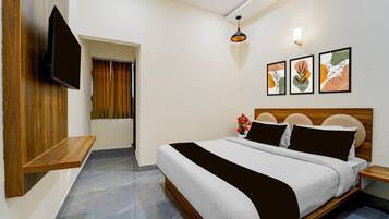 A hotel room with a bed, a TV mounted on the wall, a small wooden table, and a window with curtains.