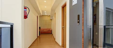 A hallway with wooden flooring, a fire extinguisher mounted on the wall, and a door with a number plate.