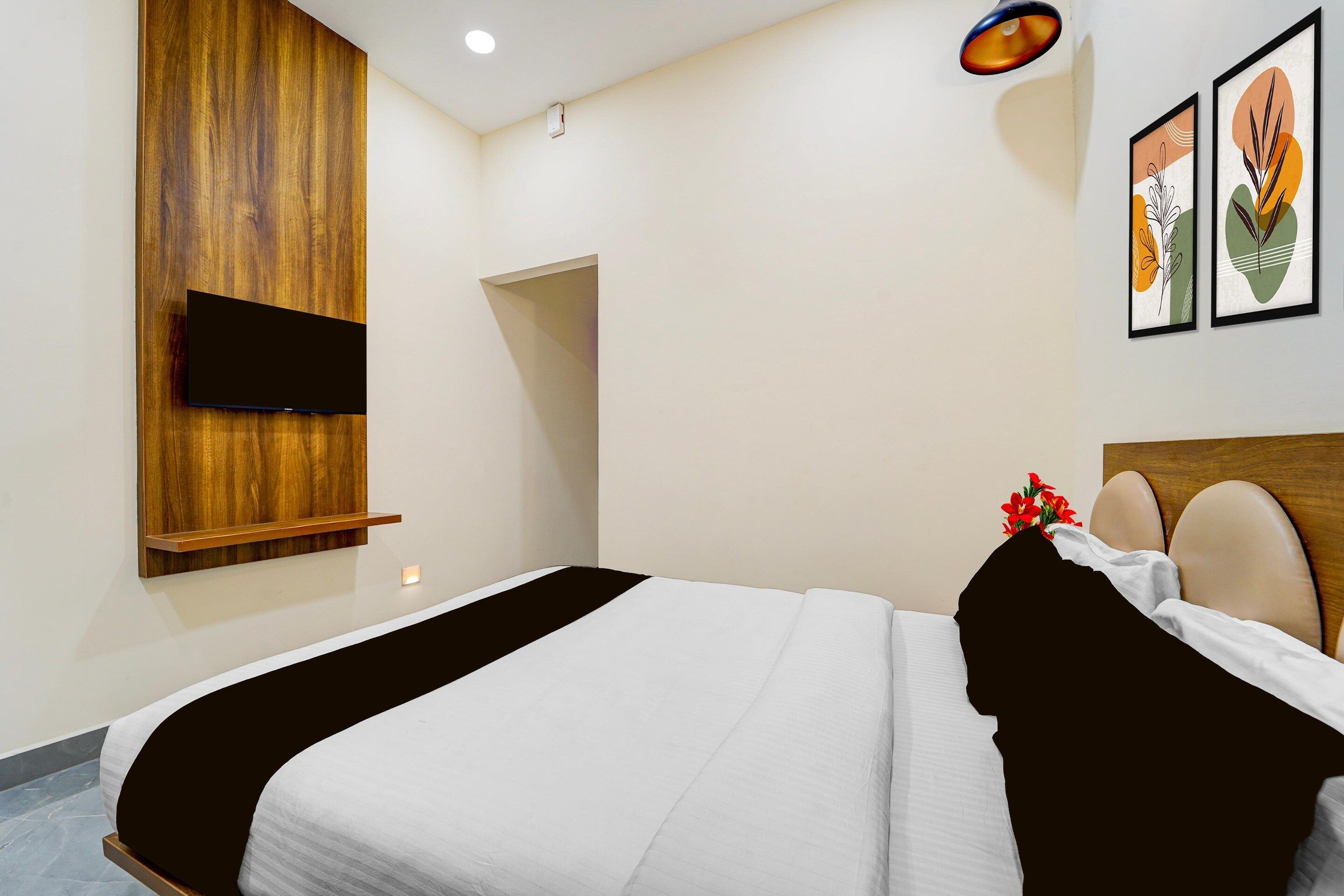 A hotel room with a bed, a mounted TV, and two framed artworks on the wall.