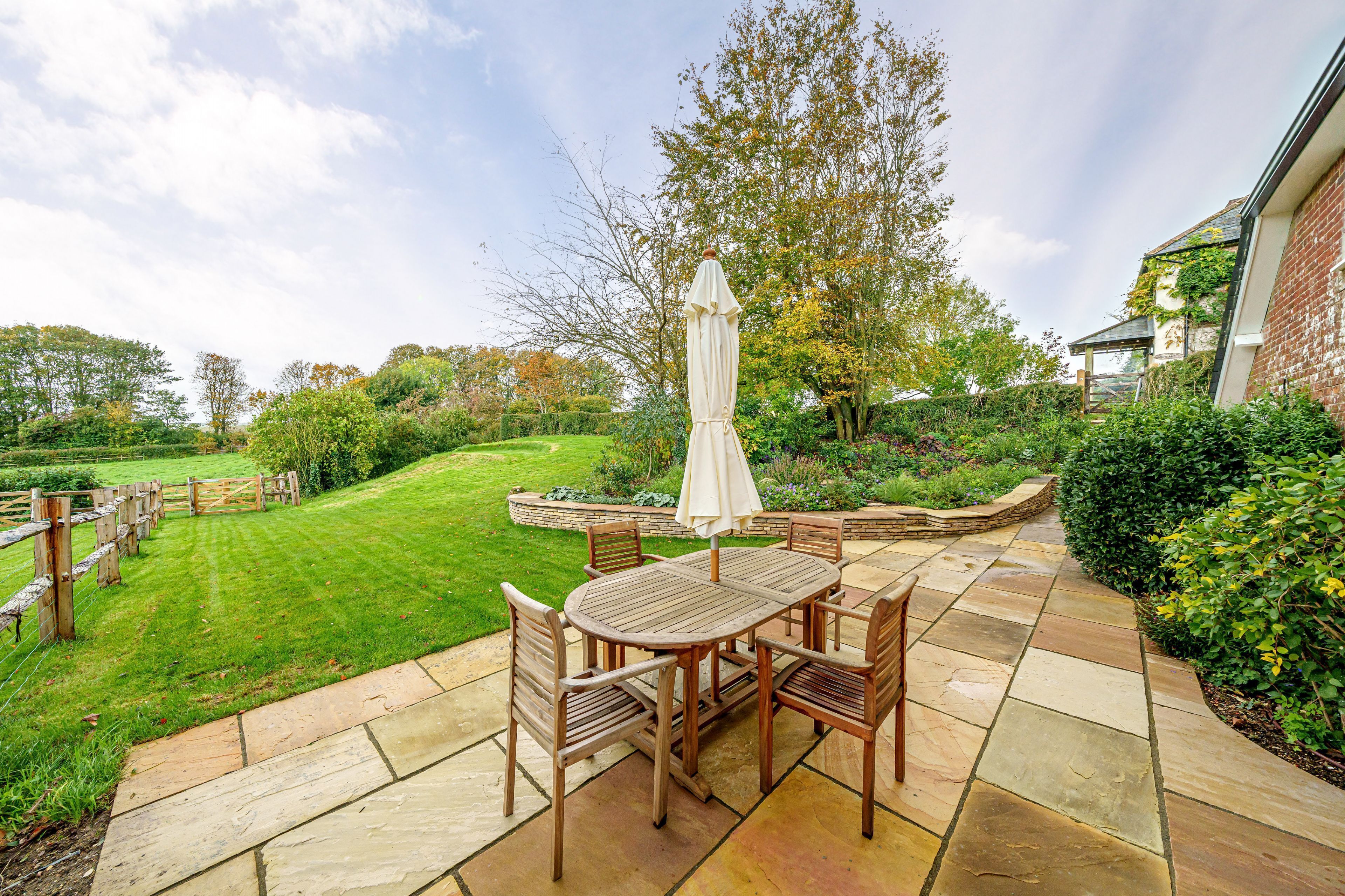 Une terrasse avec une table et des chaises, entourée d’un chemin de pierre et d’une végétation luxuriante.