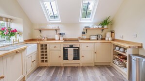 Een keuken met een centraal eiland, twee dakramen, houten werkbladen en een inbouwoven.