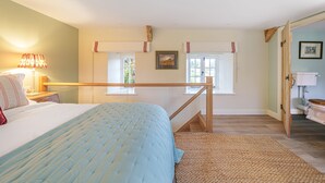 Een slaapkamer met een bed, nachtkastje, lamp, raam en deur naar een badkamer.