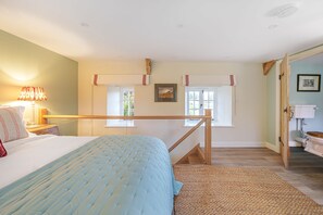 A bedroom with a bed, a nightstand, a lamp, a window, and a door leading to a bathroom. - Puddle Cottage  -  Chebbard, Dorchester (Chebbard)