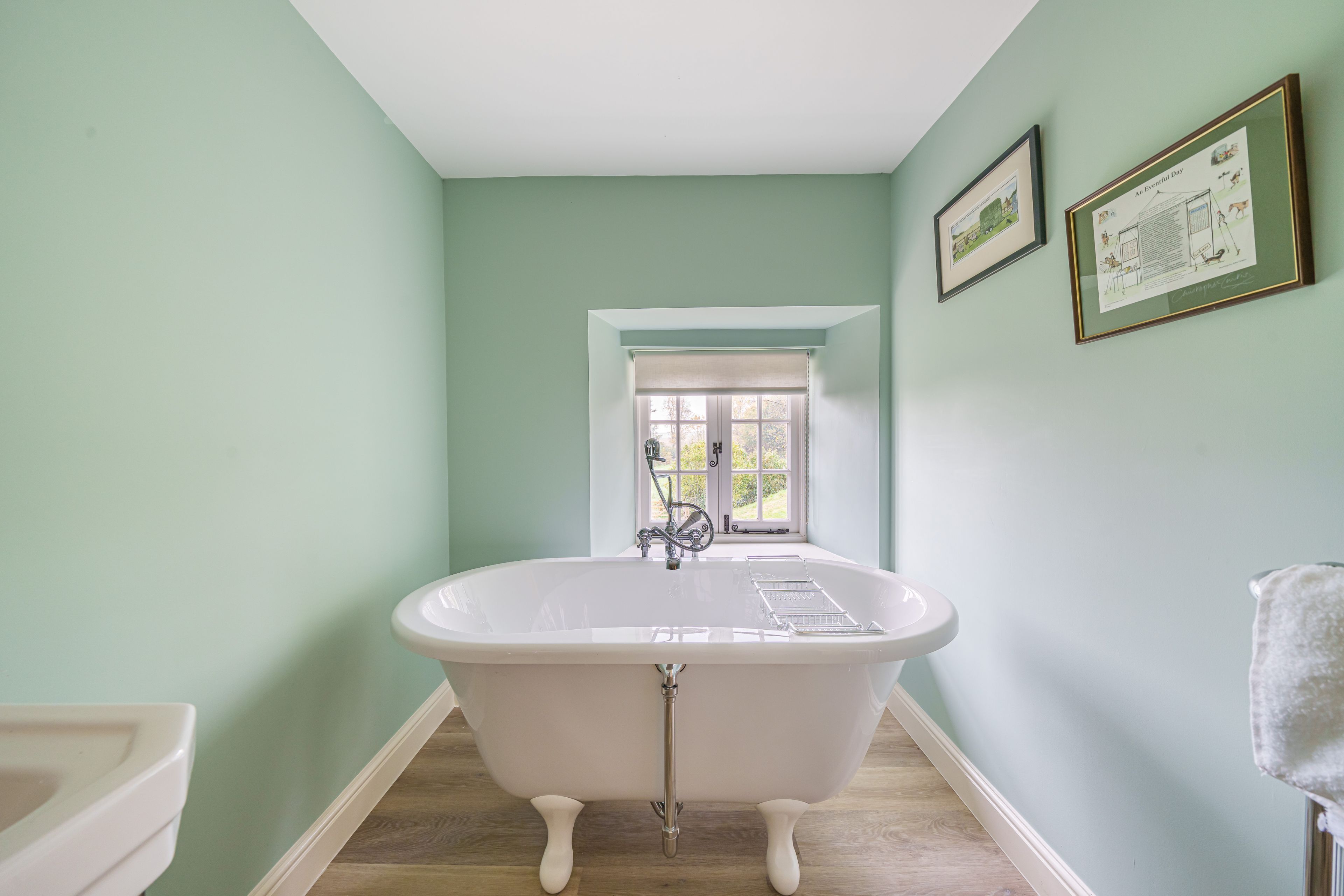 Une salle de bain avec une baignoire sur pieds, une fenêtre donnant sur un paysage verdoyant et deux tableaux encadrés accrochés au mur.