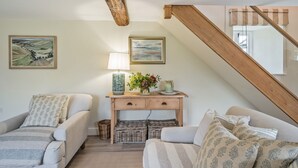 Un salon chaleureux avec deux canapés, une console en bois agrémentée d’objets décoratifs et un escalier.