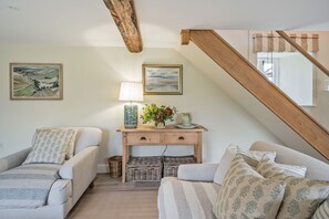 A cozy living room with two sofas, a wooden console table with decorative items, and a staircase. - Piddle Cottage  -  Chebbard, Dorchester (Chebbard)