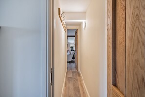 Ein Flur mit Holzboden, einem Kleiderständer und einer Tür zu einem Zimmer mit einem Bett und einer Lampe.