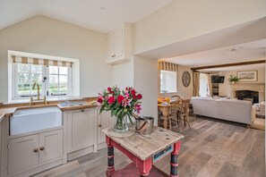 A kitchen with a wooden table and a vase of flowers, a dining area with a table and chairs, and a living room with a sofa and fireplace. - Piddle Cottage  -  Chebbard, Dorchester (Chebbard)