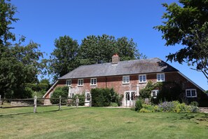 Une grande maison en briques, dotée d’un toit à forte pente, de nombreuses fenêtres et d’une cheminée.