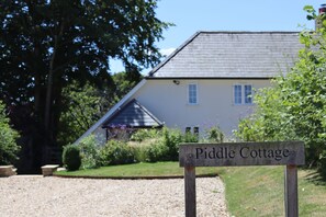 A sign for Piddle Cottage with a gravel path leading to a house with a sloped roof and a garden in the foreground. - Piddle Cottage  -  Chebbard, Dorchester (Chebbard)