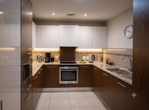 A modern kitchen with stainless steel appliances, a built-in oven, and a sink with a dish rack. - 2-bedroom apartment Cape Royale Luxury Suite (Cape Town)