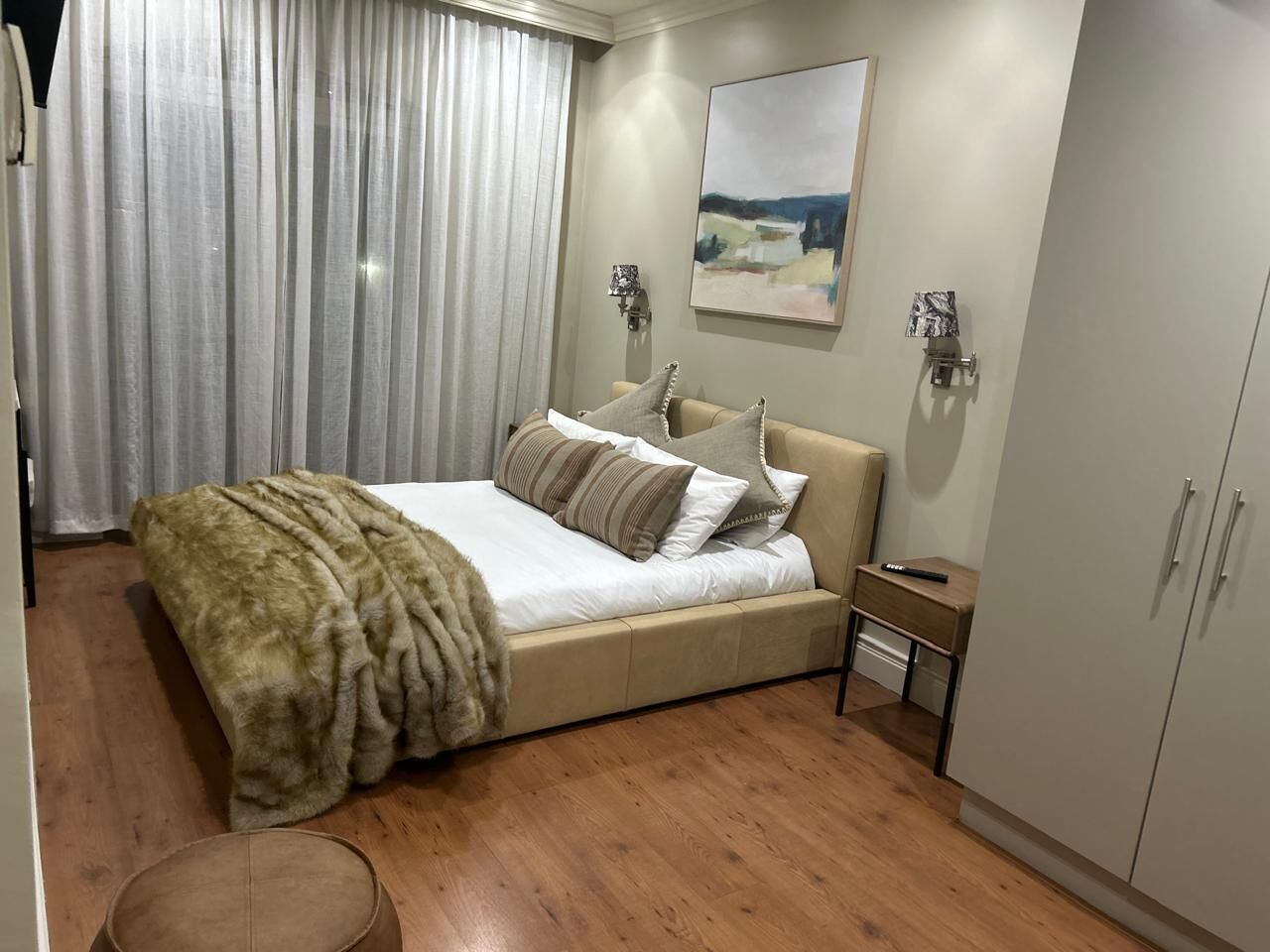 A bedroom with a bed, a nightstand, a wardrobe, and a painting on the wall.