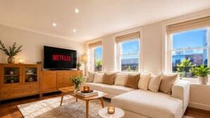 Uma sala de estar moderna com um sofá, mesa de centro e TV exibindo 'NETFLIX'.