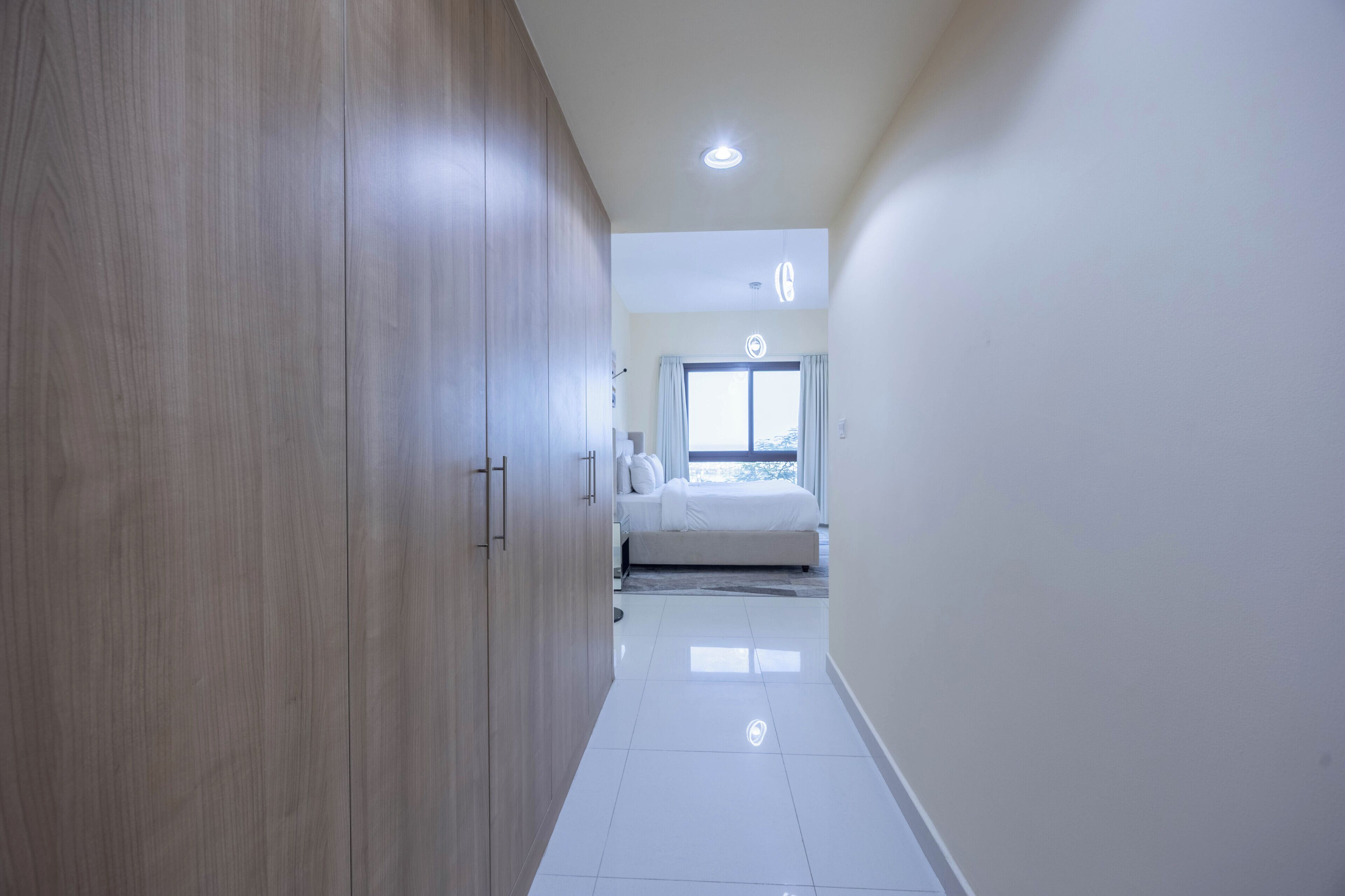 A hallway leading to a bedroom with a bed, a window, and a wardrobe.