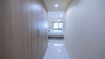 Corredor que dá para um quarto com cama, janela e guarda-roupa.