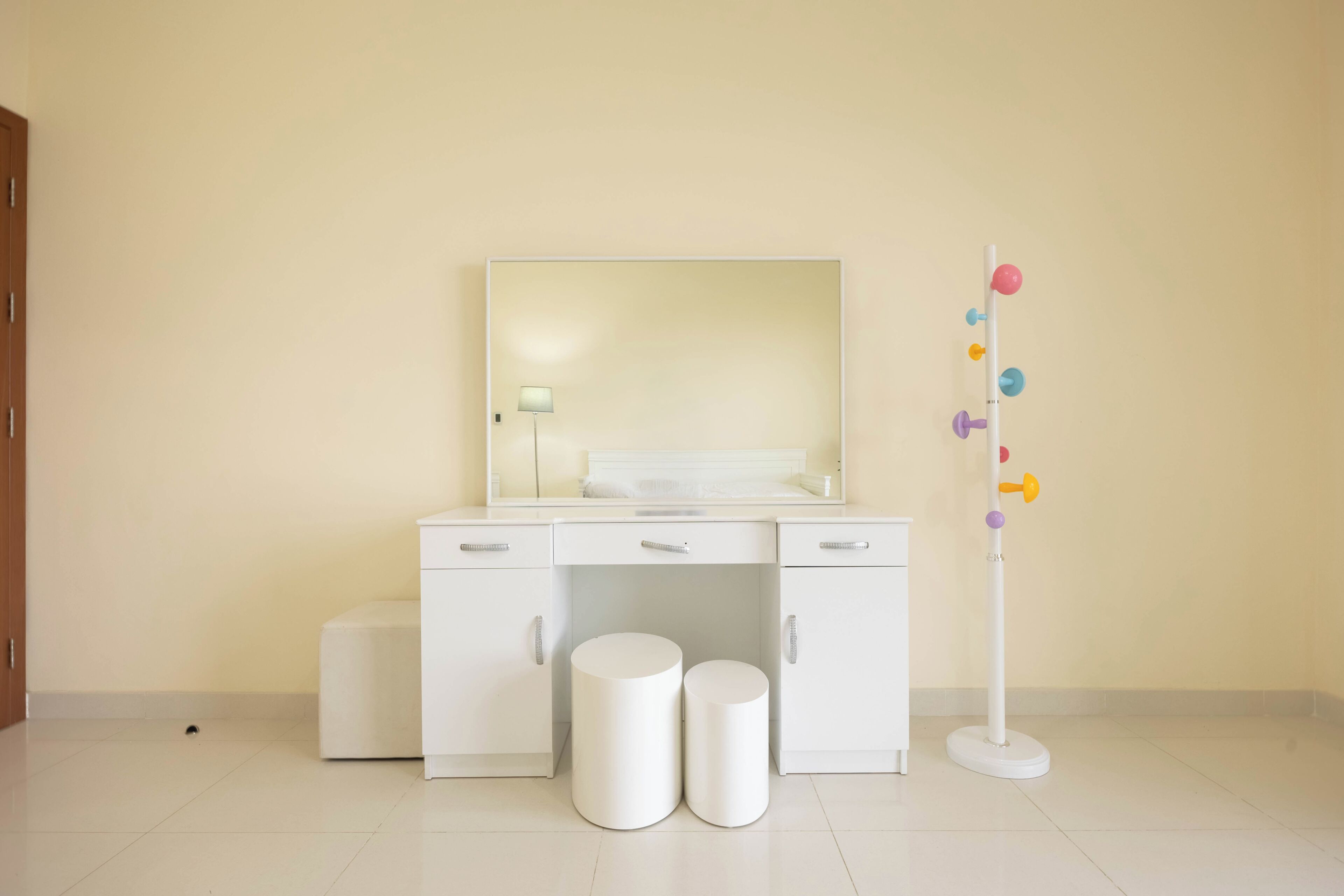 A room with a white vanity, two round stools, a mirror, and a wall-mounted pegboard with colorful hooks.