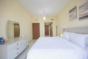 Ett hotellrum med en stor säng, en byrå, en spegel, en klädställning och en dörr som leder till ett annat rum.